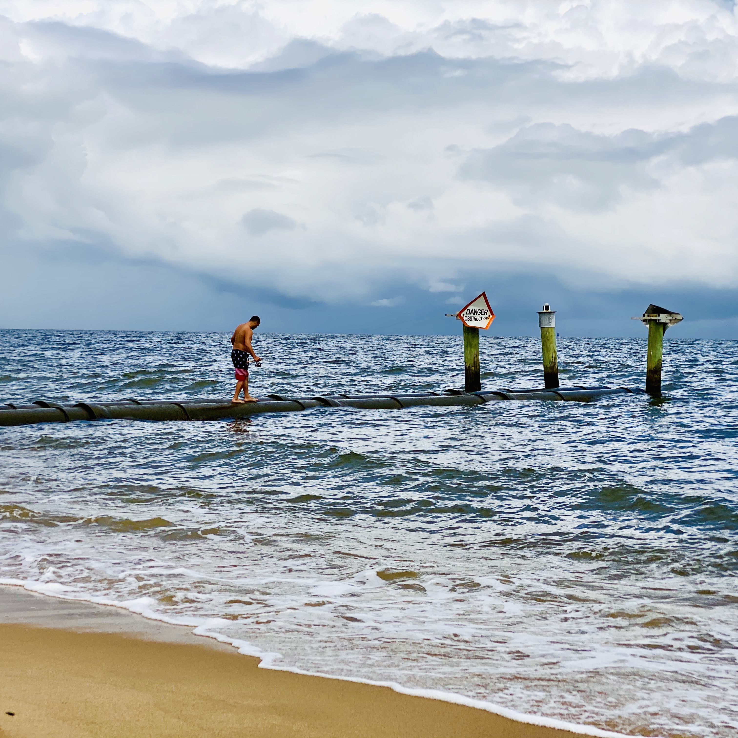 Man walking walking along barrier in the ocean