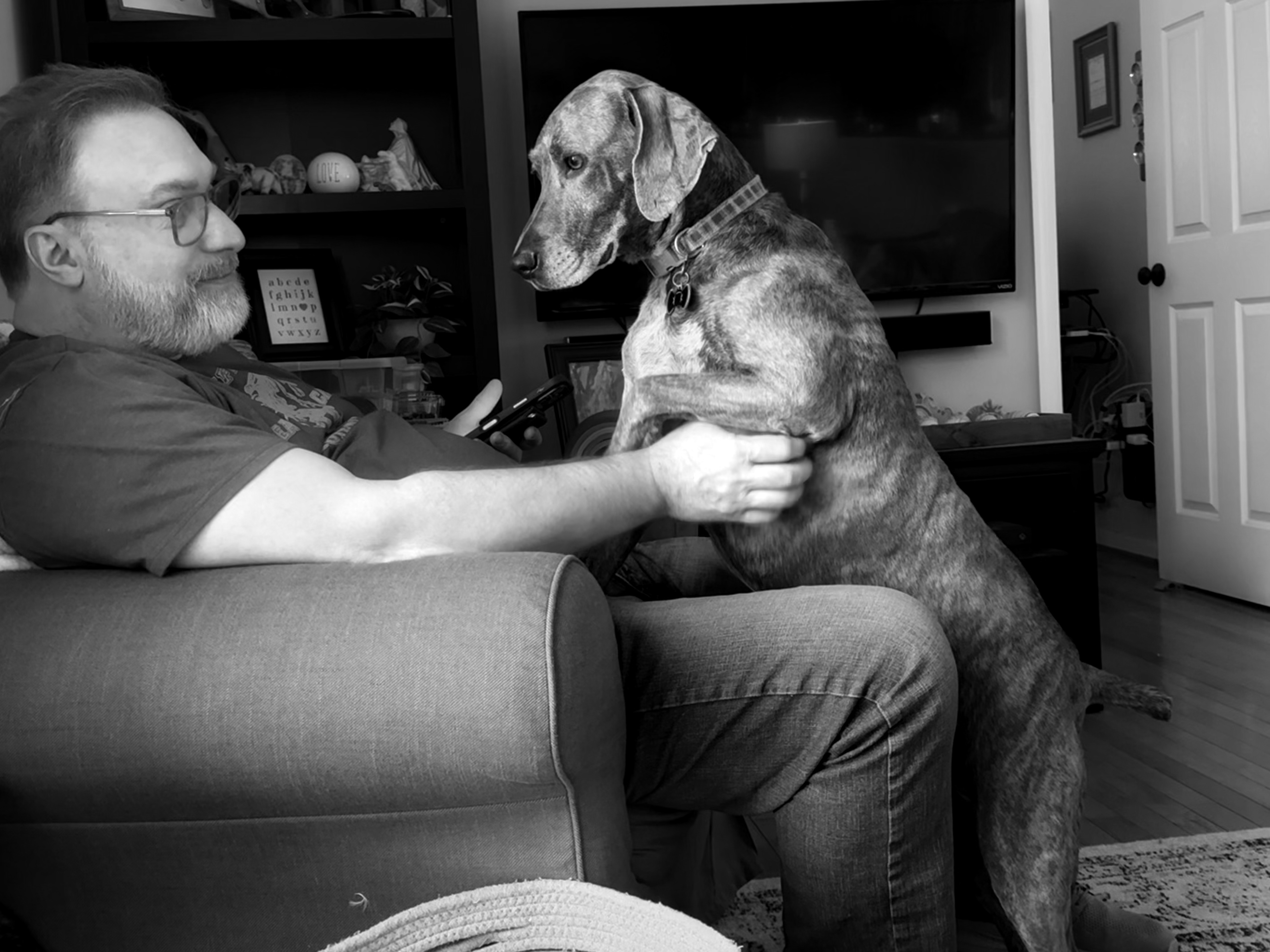 Black and white photo of a man and dog looking at each other while the man scratches the dog's side. 